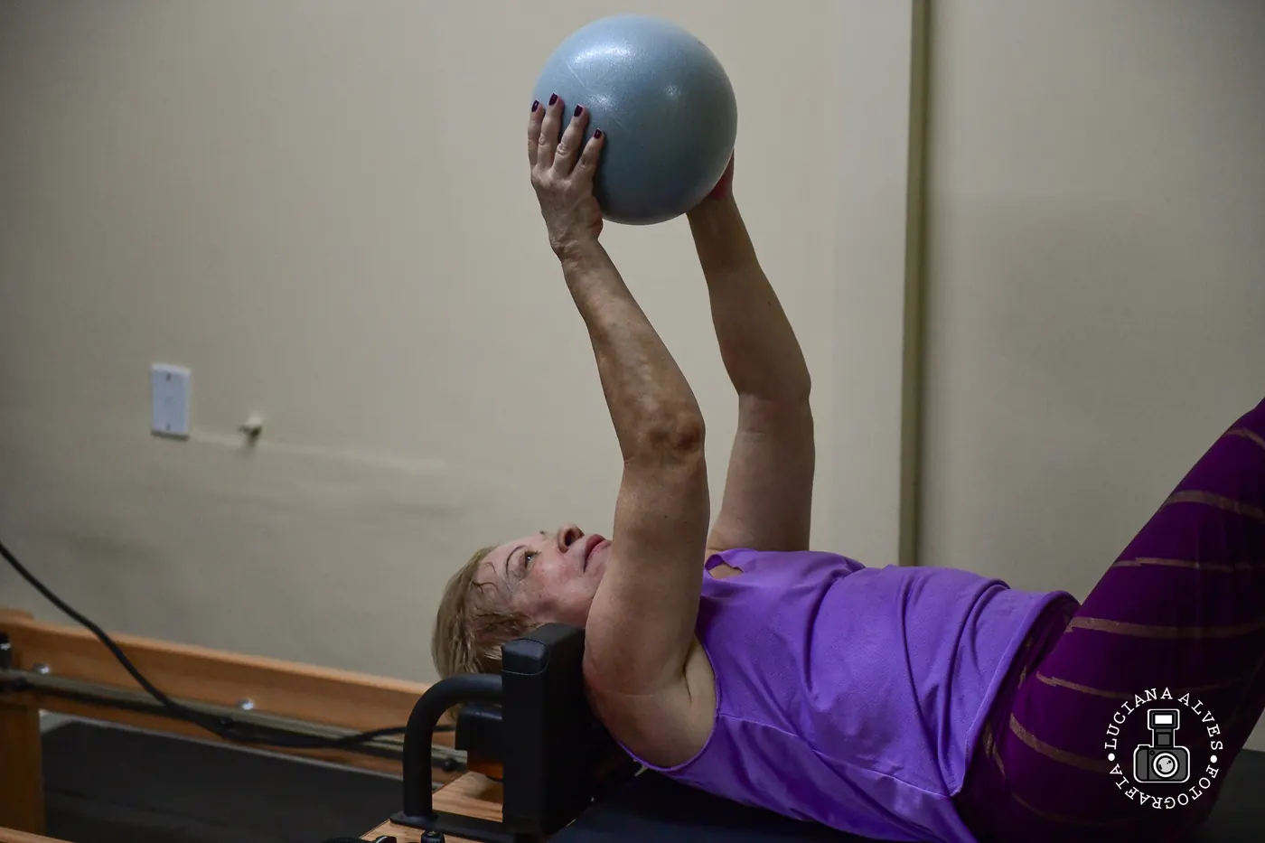 Aluna em exercício com bola no reformer na sala de Pilates